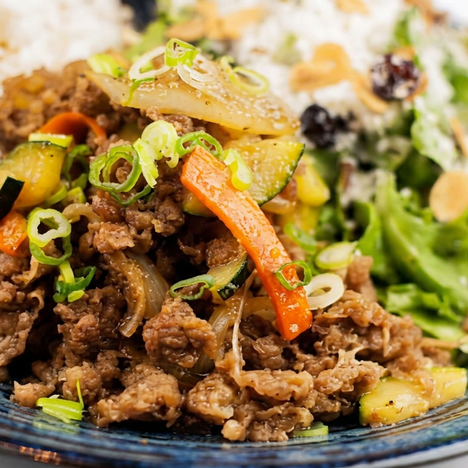 Korean-style beef stir-fry with vegetables and scallions served alongside white rice and salad on a blue plate.